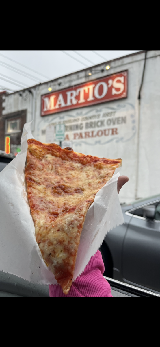 A Martios pizza slice being held up to showcase its glory, drenched in the natural parking lot sunlight, just moments before being devoured. 