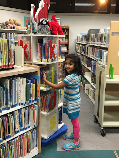 A young Ancelin Mathew eagerly peruses the library shelves in search of her next book.  